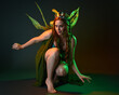 © faestock - portrait of female model wearing fantasy fairy costume, green dress, cloak, butterfly wings and crown. full length sitting pose, kneeling on floor, dark studio background.