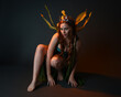 © faestock - portrait of female model wearing fantasy fairy costume, green dress, cloak, butterfly wings and crown. full length sitting pose, kneeling on floor, dark studio background.