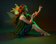 © faestock - portrait of female model wearing fantasy fairy costume, green dress, cloak, butterfly wings and crown. full length sitting pose, kneeling on floor, dark studio background.