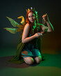 © faestock - portrait of female model wearing fantasy fairy costume, green dress, cloak, butterfly wings and crown. Full length kneeling pose holding secret jewellery box, isolated on dark studio background