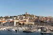© Simplementbeau. - Ville de Marseille, vue sur le Vieux Port avec des bateaux à quai en premier plan et la basilique Notre Dame de la Garde sur la colline en arrière plan, bâtiments anciens et grand ciel bleu