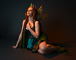 © faestock - portrait of female model wearing fantasy fairy costume, green dress, cloak, butterfly wings and crown. full length sitting pose, kneeling on floor, dark studio background.