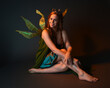 © faestock - portrait of female model wearing fantasy fairy costume, green dress, cloak, butterfly wings and crown. full length sitting pose, kneeling on floor, dark studio background.