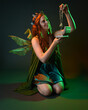 © faestock - portrait of female model wearing fantasy fairy costume, green dress, cloak, butterfly wings and crown. Full length kneeling pose holding secret jewellery box, isolated on dark studio background