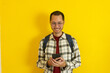 © Tito Rollis - Young man with eye glass and flannel with backpack looking smartphone on isolated yellow