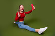 © deagreez - Happy young woman taking a selfie while sitting on a green studio background wearing a red top and jeans