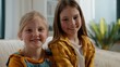© Yuliia - Portrait two happy Caucasian sisters siblings smiling joyful relaxing on couch looking at camera at home cheerful children little girls daughters kiss smile posing in living room together good family