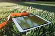 © Natalia - A tablet displaying a map lies on grass next to a measuring tape and two push pins, suggesting outdoor planning or landscaping work.