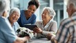 © Premium_art - Smiling young Black woman shares a tablet with joyful elderly women in a warm setting.