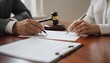 © dang - Two individuals, a man and a woman, sign legal documents on a wooden desk with a judge's gavel placed in the background.