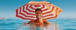 © Georgii - Smiling man swimming in the ocean holding a red striped umbrella on a sunny day
