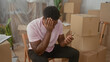© Krakenimages.com - Man holding smartphone and checking the screen, hand on face while seated among stacked cardboard boxes inside a building; moving stress.