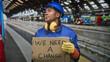 © Krakenimages.com - Man construction worker in blue coveralls and hardhat holds cardboard protest sign reading we need a change, grips wrench and wears yellow ear muffs and gloves in a building; solidarity.