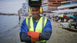 © Krakenimages.com - Man welder in welding helmet, reflective vest and gloves smiling with arms crossed on a sandy beach by a building; confidence skill duty.