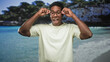 © Krakenimages.com - Man adjusting eyeglasses and smiling in studio while facing camera, hands on frames at temples, wearing casual t shirt and standing before a beach backdrop; joy vacation ease.