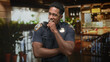 © Krakenimages.com - Man police officer holds radio mic and shows badge, smiling in restaurant interior inside a building, short sleeve uniform visible; duty service approachable.