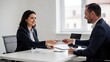 © olga_demina - A receptionist and colleague interact in a modern office setting, exchanging a business card across a white desk with natural light pouring in from a nearby window.