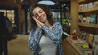 © Krakenimages.com - Woman hands to cheek for sleep in library among bookshelves, eyes closed with a mild smile, wearing patterned shirt and tank top; calm rest.