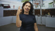 © Krakenimages.com - Woman points finger at basketball hoop by building wall, smiling with raised arm visible; confidence celebration.