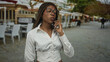 © Krakenimages.com - Woman with braided hair and glasses holds phone to ear on street outside restaurant terrace, eyes closed and hand near jawline; quiet contemplation.