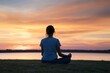 © homeganko - Sunset Meditation by the Water With a Person in a Striped Shirt Sitting on Grass