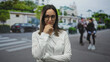 © Krakenimages.com - Woman in white shirt and glasses, palm up presenting with one hand then hand to chin pensive pose on an urban street crosswalk; thoughtful decision.