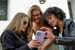 © ADDICTIVE STOCK - Diverse young women connecting with smartphone outdoors