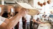 © Stitch - Professional pizza baker catching raw spinning dough in the air in a bustling commercial kitchen