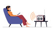 © Rocky - Relaxed woman sitting in a comfortable purple chair and listening to a vintage radio while wearing orange headphones at home.