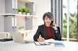 © Fahng - Happy smiling mature middle aged business woman, 50s professional lady executive manager talking on the phone making business call on cellphone and taking note at work in office .