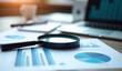 © miracle - Close up of magnifying glass over financial charts and graphs with laptop and soft lighting creates an office
