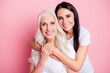 © deagreez - Mother and daughter embracing and smiling together in a casual portrait on a pink background showing family love and generational bond