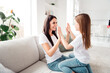 © deagreez - Mother and daughter playing hand clapping game together at home, smiling and bonding on a bright living room couch
