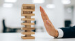 © Jabalenour - Businessman hand stopping falling wooden blocks for risk management
