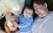 © Anna - Portrait of a young joyful family, mother and father with a cute baby, lying next to each other, view from above. Happy parents playing with their child. The concept of happy parenting