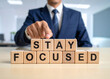 © magele-picture - Stay focused - Geschäftsmann zeigt auf den Text 'Stay focused'