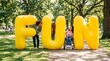 © ryker - Three diverse friends laugh together outdoors holding giant yellow letters spelling FUN, wheelchair user included, sunny park scene conveying joy and inclusive friendship