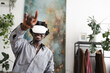 © Studio Marmellata - A young man wearing a virtual reality headset smiles as he reaches out his hand, engaging with an immersive digital experience in a modern, plant-filled room.