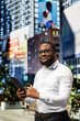 © DC Studio - African american guy browsing tablet while he walks across busy sidewalk, capturing the modernity and dynamic lifestyle of urbanism framed by sunlight and a lively vibrant city life.