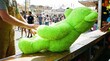 © Stitch - Worker placing a large bright green plush bear prize on the counter at a carnival game
