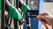 © mlangsen - Hand holds 'PAY NOW' card to fuel pumps, suggesting easy payment for gas