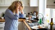 © Elisabete - Stressed woman holding her head in a messy kitchen with dirty dishes.