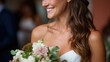 © GATE 22 - Close-up portrait of a young woman with long, wavy brunette hair. she is wearing a white strapless wedding dress and is holding a bouquet of white and pink flowers.
