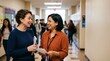 © Eve - Two diverse female teachers or colleagues talking and laughing in school hallway corridor during break time education professional concept