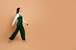 © deagreez - Confident woman walking in a green suit on a neutral studio background, side view of a stylish professional in heels