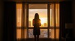 © Sean Hoong - A woman stands in a large window overlooking a cityscape at sunset, her back to the camera. She is dressed in a black dress and is holding a small object in her hand.