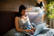 © Davor - Young woman working on laptop in bed at home