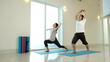 © Meng_Dakara - Man and woman practicing warrior yoga variation with arm extension at home, improving strength, balance and flexibility, enhancing full body coordination in bright minimalist indoor fitness space
