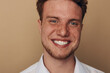 © SHOTPRIME STUDIO - Close-up portrait of a smiling young man with freckles and red hair on beige background. Concept of happiness, confidence, and natural beauty in casual style.