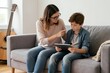 © Lubov - Mother scolds boy holding tablet computer. Woman points finger, child looks unhappy. Parenting conflict at home on sofa. Family disagreement about screen time.